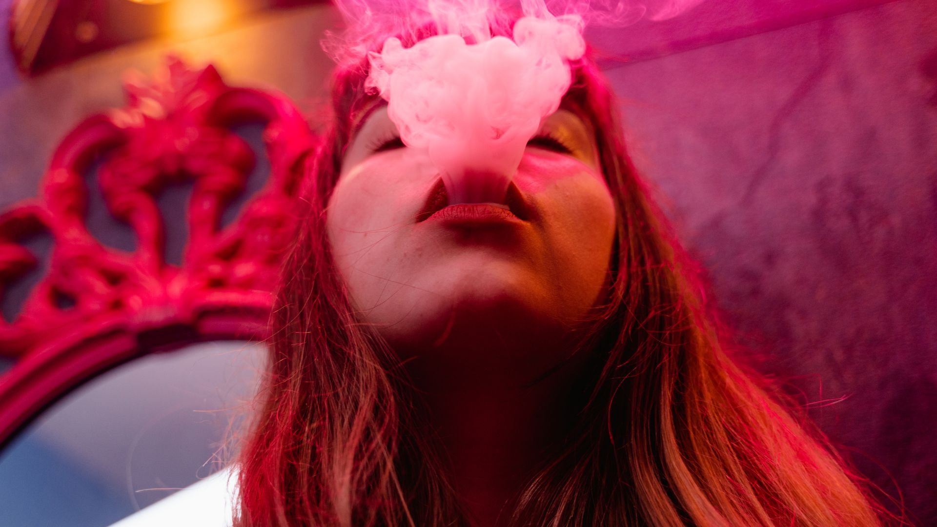 Person with pink smoke exhaling, wearing a red crown in vibrant lighting